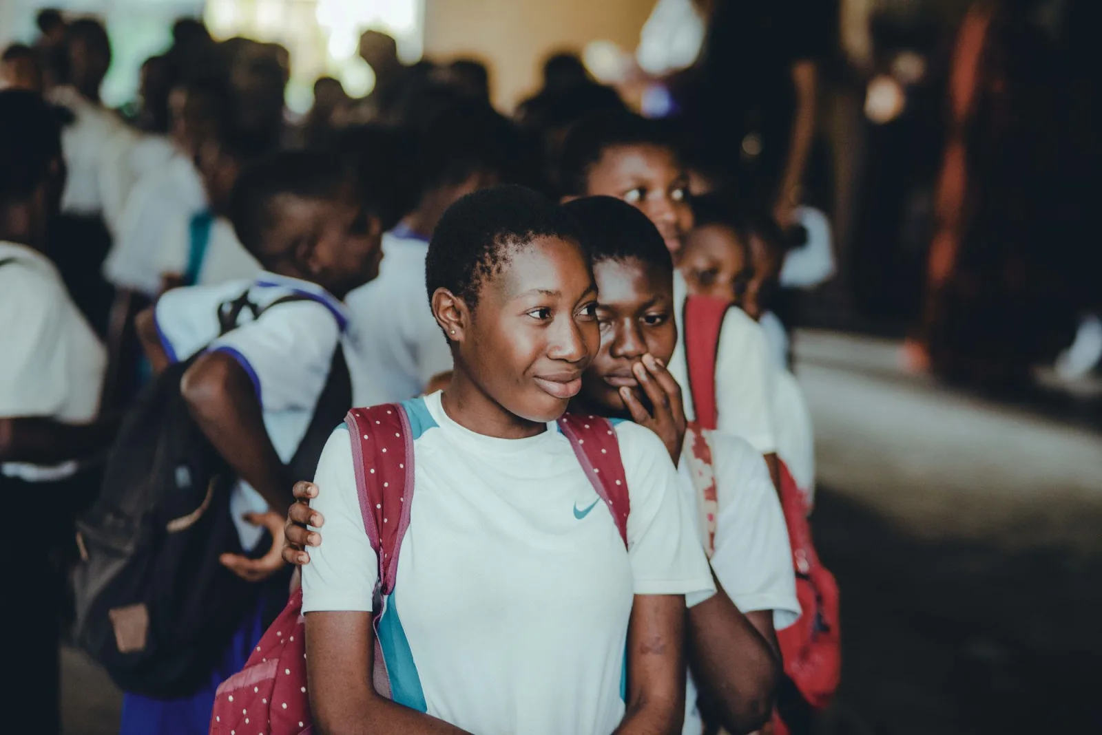 A schoolgirl with a backpack smiling among her classmates. Photo by Tosin Olowoleni on Pexels.